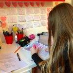 Female student revising at home with sticky notes on wall, highlighting text on paper