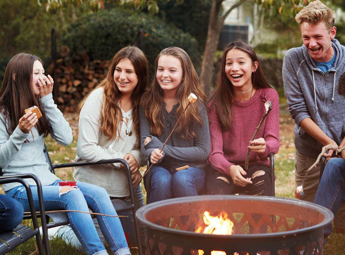 Students laughing while eating smores around a firepit